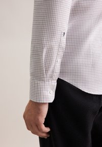 Lange mouwen shirt in een wit en beige ruitpatroon, met knoopmanchetten en een geborduurde roosdetail op de mouw.