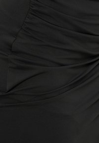 Gros plan sur un tissu noir avec une texture froncée et plissée créant de doux plis et ombres.