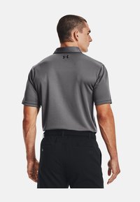 Polo grigio con finitura testurizzata, maniche corte e logo nero sul retro. Abbinato a pantaloni neri, con una vestibilità rilassata.