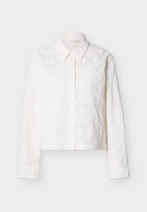 Bela, skrajšana srajca z dolgimi rokavi, z vezenim cvetličnim vzorcem in majhnim prsni žepom. Gladek tekstura.