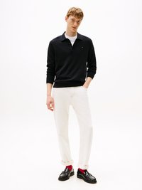 Svart langermet polo genser med krage, brukt over en hvit T-skjorte, kombinert med oppbrettede hvite jeans og svarte loafers med røde sokker.