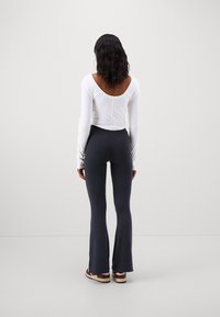 Vit nedskuren långärmad topp med vid halsringning, kombinerad med åtsittande mörkgrå utsvängda leggings och avslappnade flerfärgade sneakers.