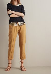 Černý krátký rukáv top navrstvený na košili s květinovým potiskem, spárovaný s hořčicovými lněnými kalhotami a hnědými sandály na pásky.