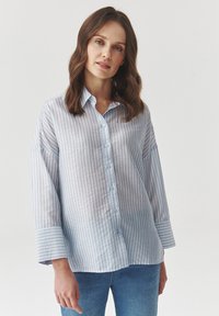 Camisa de botones a rayas azul claro con un corte relajado, que cuenta con mangas largas y una tela suave y texturizada.