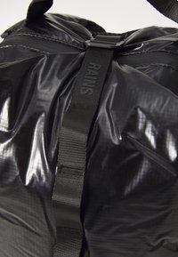Geantă din material textil negru cu un finisaj lucios, curea ajustabilă și o suprafață texturată cu modele subtile în grilaj. Accesoriile afișează numele mărcii.