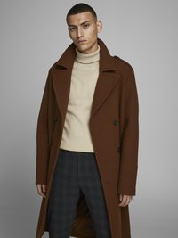 Manteau en laine brun avec un grand col et des boutons doublés, porté sur un col roulé beige et un pantalon à motifs carreaux.