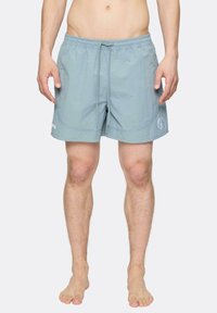 Svetlomodré plavky vyrobené z ľahkého materiálu, s elastickým pásom so šnúrkou a bočnými vreckami. Obsahuje akcent loga.