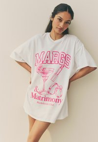 Vit oversized T-shirt med rosa grafisk text "MARGS" och illustrationer av ett cocktailglas, läppstift och vigselringar.