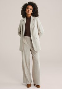 Helehall triibuline ülikond, mis koosneb hästiistuvast bleiserist ühe nööbikesega ja laiade pükstega. Riidekiht on ühtlase tekstuuriga.