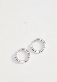 Para gładkich, błyszczących srebrnych kolczyków-koła o zaokrąglonym, rurowym kształcie na białym, jednolitym tle.