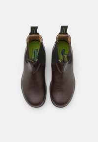 Des bottes de cheville en cuir marron présentent une finition lisse, des panneaux élastiques sur les côtés, et une semelle en caoutchouc robuste avec une semelle intérieure verte pour le confort.
