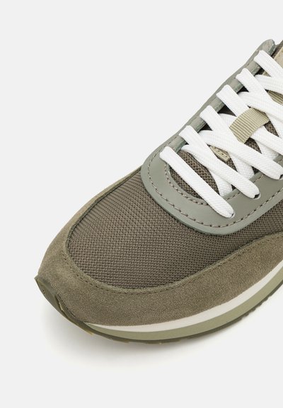 Olivgrüner Sneaker mit einer Kombination aus strukturiertem Mesh und weichem Wildleder, weißen Schnürsenkeln und einem runden Zehendesign mit einer kontrastierenden Sohle.
