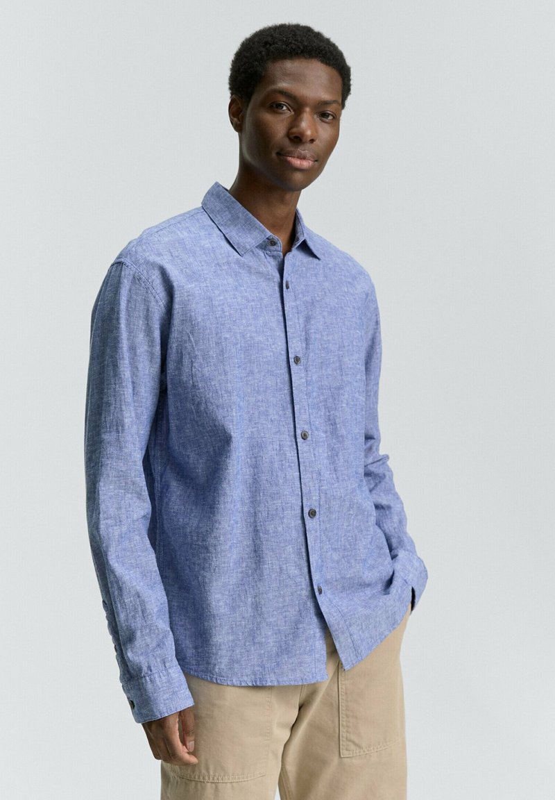 Blauwe overhemdd met een gestructureerde stof, klassieke kraag, en lange mouwen met knoopmanchetten, in combinatie met beige broek.