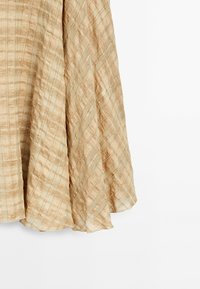 Hellbeige Rock mit einem karierten Muster und strukturierten Streifen. Der Stoff ist fließend mit einem subtilen Glanz und einem abgerundeten Saum.