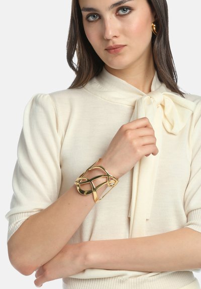 Auksinis apyrankė, pasižyminti sudėtinga susukta struktūra, su lygiomis, atspindinčiomis paviršių ir atvira struktūra, nešiojama ant riešo.