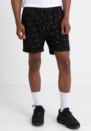 Shorts noirs à taille élastique avec cordon, arborant un motif répété de formes abstraites blanches. Confectionnés en tissu léger, ourlet roulé.