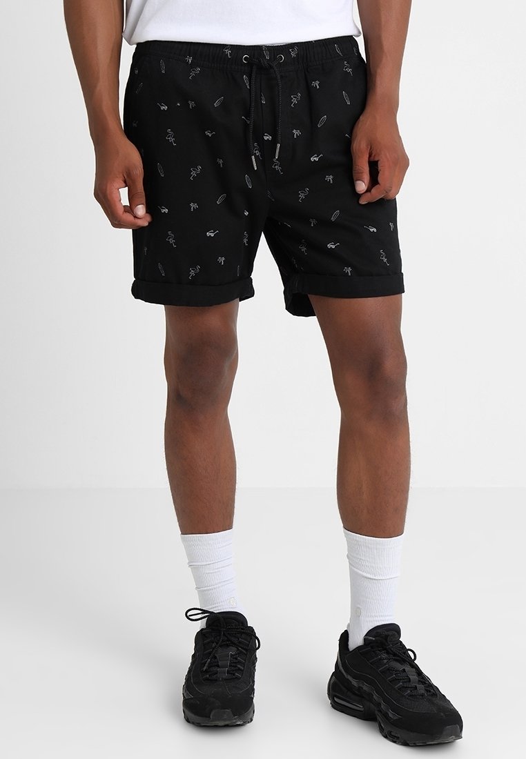 Shorts noirs à taille élastique avec cordon, arborant un motif répété de formes abstraites blanches. Confectionnés en tissu léger, ourlet roulé.