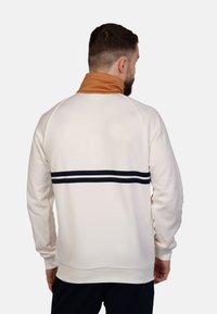 Helltöniger Sweatshirt mit hohem Kragen, der einen braunen Bereich am Hals und zwei marineblauen Horizontalstreifen über den Rücken hat.