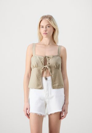 Haut en lin beige clair à manches courtes avec décolleté carré, détail de lien devant et bretelles épaisses, associé à un short en denim blanc déchiré.