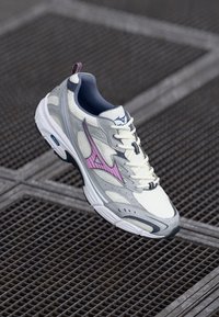 Sport shoe with a light grey and white mesh upper, pink accents, and a supportive design. Features a textured outsole and cushioned collar.