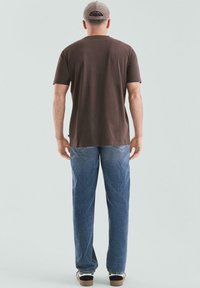 Brązowy t-shirt z krótkim rękawem o luźnym kroju, miękka w dotyku, zestawiony z niebieskimi dżinsami. Stylizację uzupełniają czarno-białe trampki.