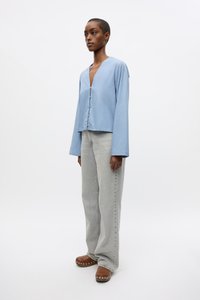Light blue, long-sleeved blouse with a deep V-neck and button closure; paired with gray wide-leg jeans and brown clogs with metallic studs.