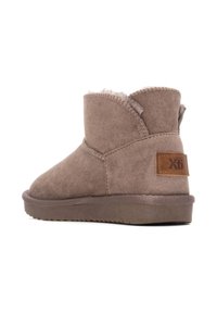 Botas de ante marrón hasta el tobillo con forro interior suave, detalles de costura y una etiqueta de cuero de marca en el talón. Suela de goma plana.