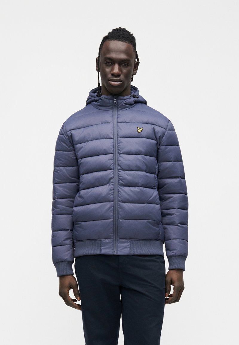 Navy padded jacket with a zip front and hood. Features a small gold logo on the left chest and ribbed cuffs and hem. Smooth texture.