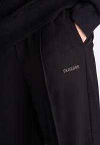 Schwarze Jogginghosen aus weichem Stoff mit lockerer Passform. Verfügt über dezente seitliche Taschen und ein gesticktes "PEGADOR"-Logo in hellgrau.