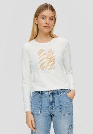 T-shirt blanc à manches longues avec un design graphique abstrait orange et bleu, associé à un jean en denim bleu clair taille haute avec des poches plaquées.