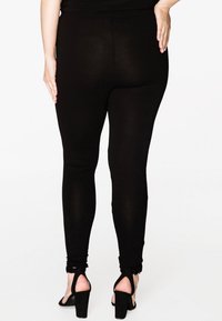 Zwarte leggings met een gladde textuur en een strakke pasvorm, met een hoge tailleband en geplooide accenten bij de enkel. Gagaan met hoge hakken.