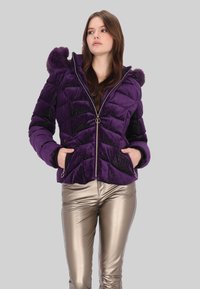 Fioletowa pikowana kurtka o błyszczącej fakturze, z wzorem w jodełkę, dwiema bocznymi kieszeniami oraz kapturem wyściełanym futrem, zestawiona z metalicznymi srebrnymi spodniami.