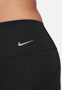 Sorte treningsshorts laget av elastisk stoff, med en flat midjebånd, en liten sølvfarget Nike-logo og sømløs konstruksjon for komfort.