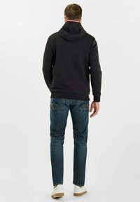 Svart hoodie med dragsko i huvan, tillsammans med blå denimjeans. Skorna är beige och vita sneakers. Utsikten visar baksidan av outfiten.