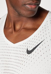Weißes ärmelloses Sportshirt mit V-Ausschnitt, perforiertem Stoff und schwarzem Nike-Logo auf der linken Seite.