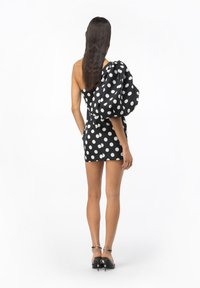 Abito nero con pois bianchi, una manica a sbuffo, corpetto aderente e orlo corto. Tessuto liscio con pois bianchi a contrasto, design minimalista.