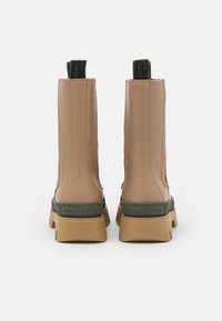 Une paire de bottes beiges mi-mollet avec des semelles épaisses couleur tan, des bandes de talon vertes embossées avec "Marc O'Polo", et des chevilles en tissu noir à l'arrière.