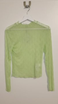 Long-sleeve top in sheer, light green fabric with subtle wave patterns. Rounded neckline and slightly loose fit, hanging on a white hanger.