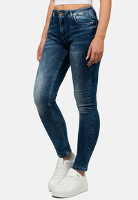 Jeans skinny blu con un design sbiadito, dotati di chiusura con zip e bottone, tasche frontali e gamba affusolata. Indossati con sneakers bianche.