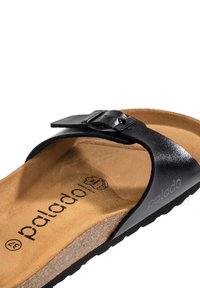 Sandales flip-flop en cuir noir avec une accent dorée, semelle en liège et semelle en caoutchouc texturé. Présente le logo de la marque sur la semelle intérieure.