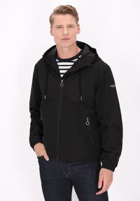 Zwarte gewatteerde jas met een rits aan de voorkant, een trekkoord en twee voorke pocket. Draagt over een gestreept shirt en gecombineerd met donkere jeans.