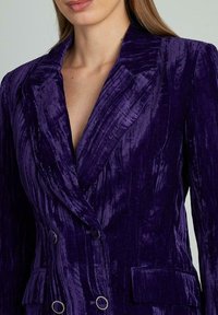 Giacca doppiopetto in velluto viola con strisce verticali, bottoni metallici, revers a scialle e tessuto testurizzato, che esalta un design elegante.