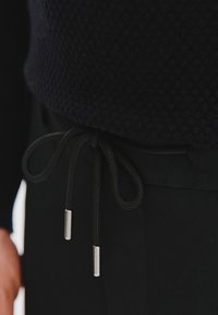 Czarne spodnie z teksturowanym ciemnym swetrem, z paskiem ze sznurkiem i metalowymi końcówkami, tworzącymi elegancki i funkcjonalny design.