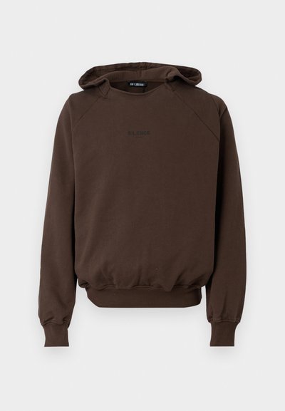 Smeđa kapuljača s raglan rukavima, rebrastim manžetama i donjim rubom, s malim crnim logom "SILENCE" na prsima. Mekana tekstura.