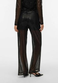 Mustast litrilisest võrgukangast kombinesoon, millel on pikad varrukad, mustrilised teemandid, läbipaistev kangas, lahtine lõige, kombineeritud teravnurksete mustade kontsakingadega.