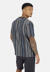 Szaro-czarna, pasiasta koszulka z krótkim rękawem, z niebieskimi akcentami, o okrągłym dekolcie i luźnym kroju. Widoczna wzorzysta faktura.