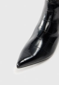Stivaletti neri a punta con texture coccodrillo, caratterizzati da una finitura lucida e da una silhouette elegante. Il tacco è sottile e affusolato.