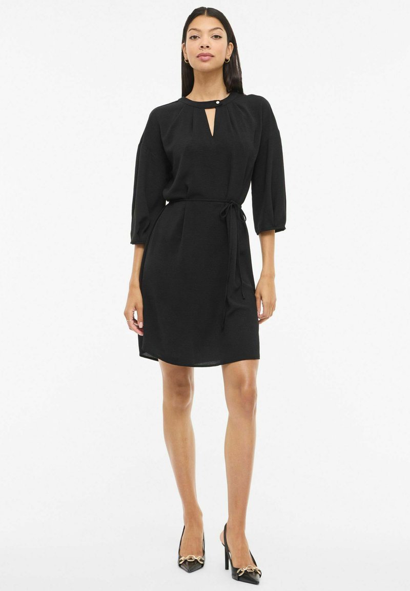 Czarna sukienka z okrągłym dekoltem, wycięciem z przodu, rękawami do łokcia i wiązanym paskiem w talii. Gładka tkanina o luźnym kroju.