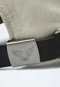 Bandeau de casquette en textile beige avec une sangle en cuir noir et un fermoir en métal argenté arborant un logo ailé.