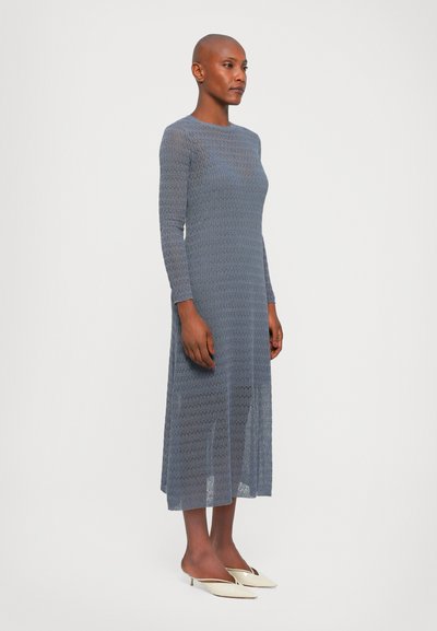 Rochie cu mânecă lungă, de lungime midi, dintr-un material tricotat de culoare albastru deschis, cu un model texturat. Asortată cu pantofi slip-on de culoare albă.
